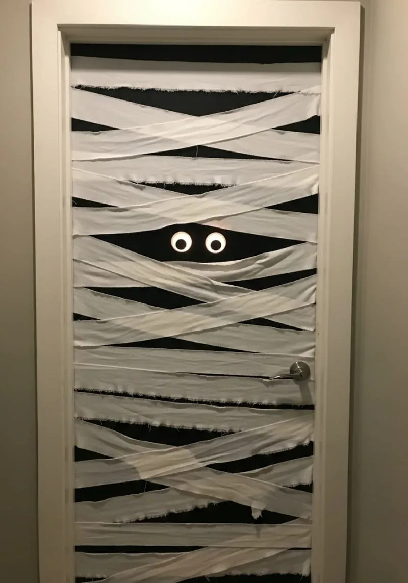 21 Creative Halloween Door Decorations: Ideas for a Festive Welcome 14 mummy door with googly glowing eyes peeking through white bandages 1