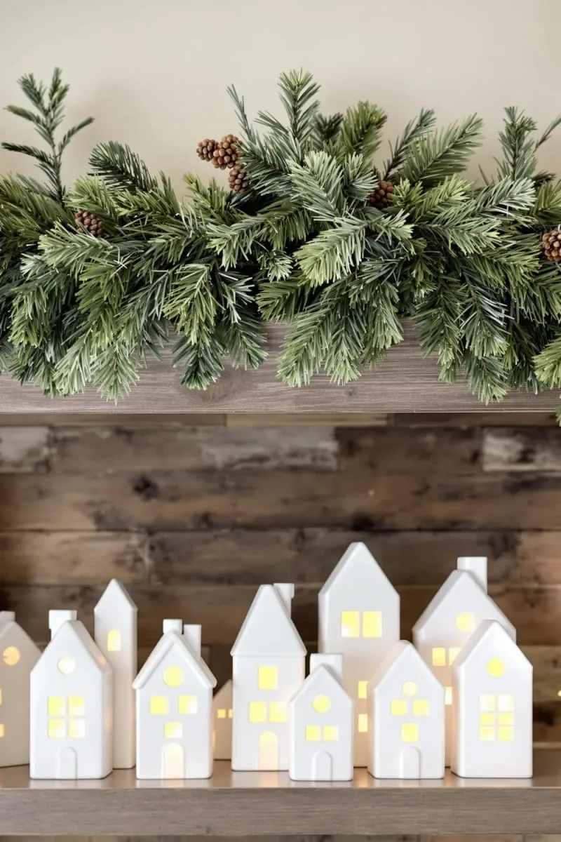 white ceramic houses glowing softly beneath a pine branch swag 1