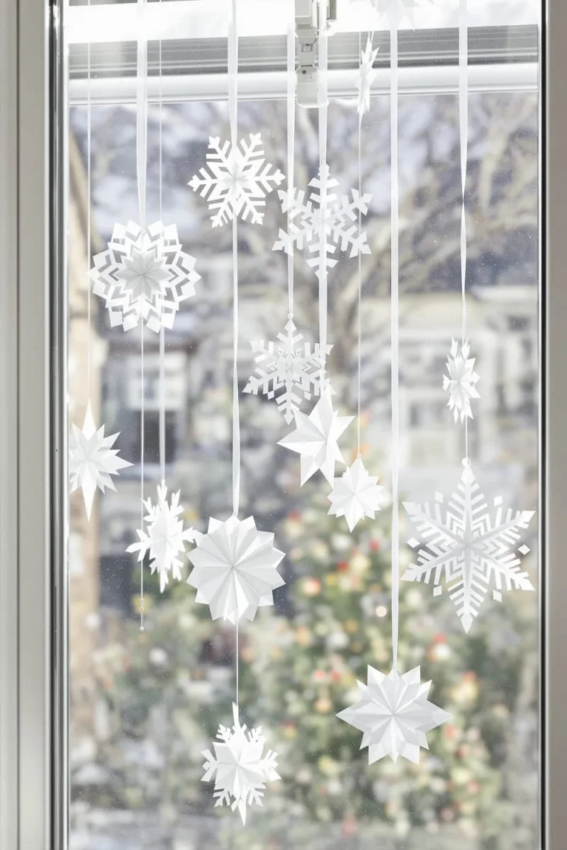 29 Simple Christmas Decor Ideas for a Beautiful Holiday Season 31 white origami snowflakes hanging in front of a window 1