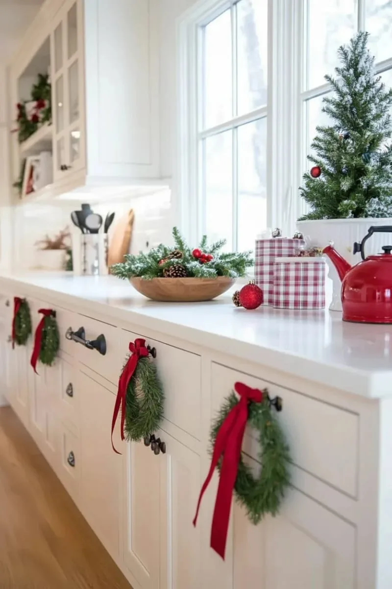 mini evergreen wreaths hanging from red satin ribbons on cabinet handles 1