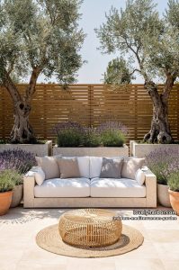 outdoor patio with white sofa, olive trees, lavender planters, rattan ottoman, and privacy fence. 42