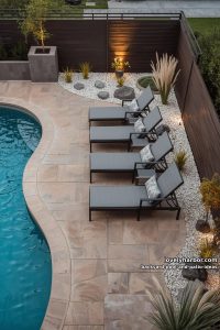 freeform pool, textured deck, gray lounge chairs, white gravel, modern landscaping, privacy fence. 16