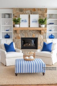 20 Coastal Living Rooms to Refresh Your Space 1 cream armchairs, striped ottoman, blue accents, and stone fireplace in coastal living room. 18