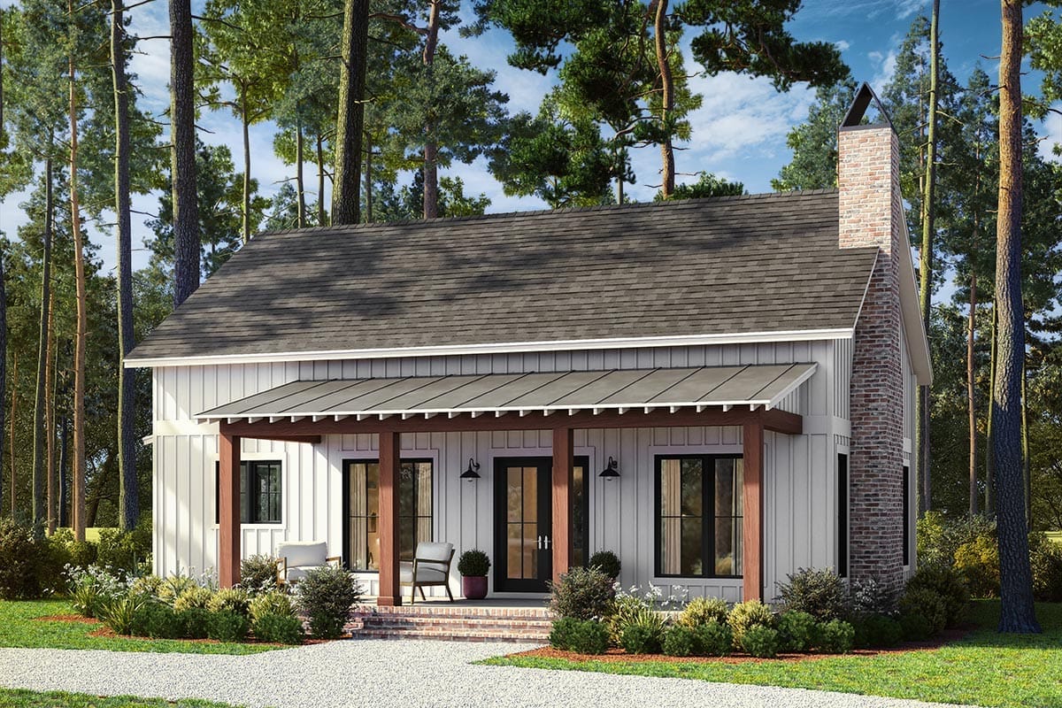 Front view of a 2-bedroom barndominium cottage house plan featuring a white board and batten exterior, brick chimney, covered porch with wooden posts, and surrounding landscaping, representing a 1,320 sq. ft. floor plan.