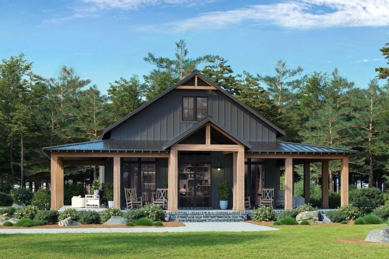 Front view of a 3-bedroom barndominium house plan featuring a wrap-around porch, dark metal roof, wooden columns, large windows, and surrounded by trees and landscaped greenery.