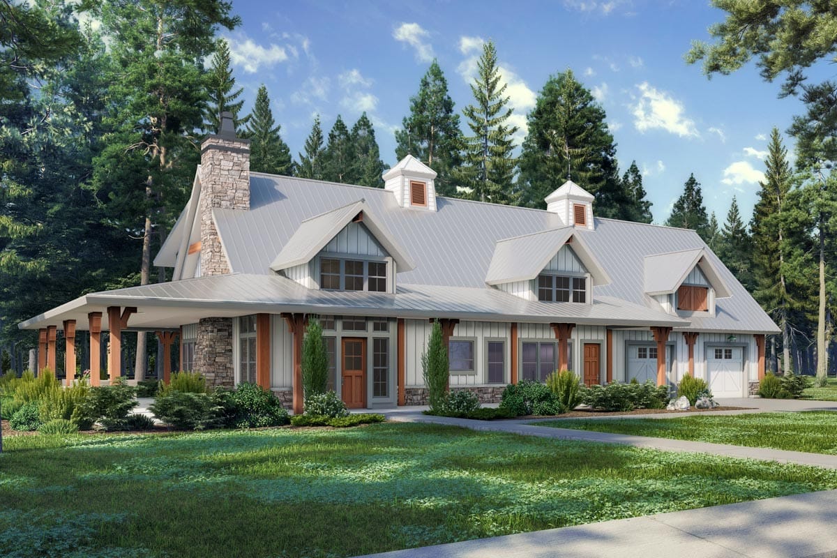 Farmhouse-inspired home with metal roof, dormers, wraparound porch, and stone accents in wooded setting.