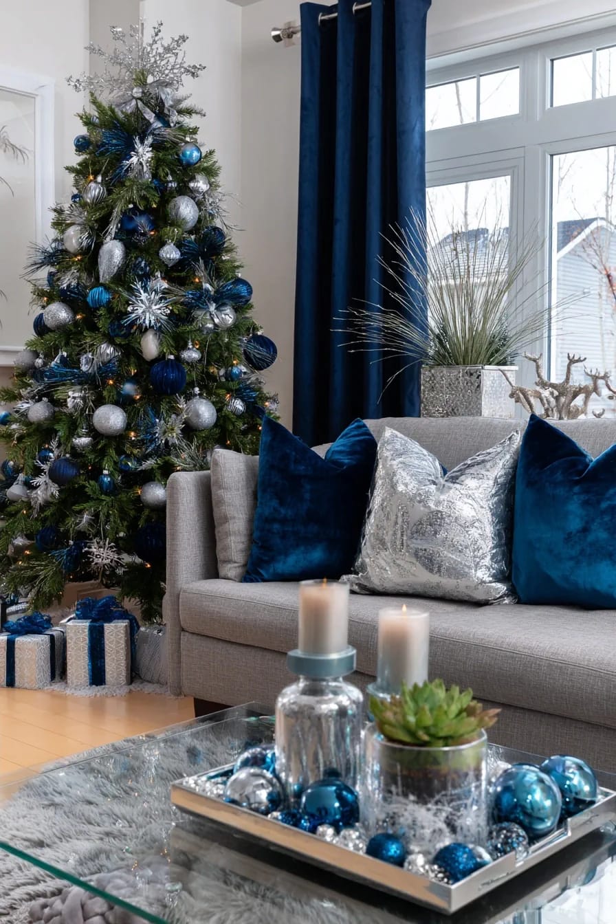 Blue and Silver Christmas Decor Ideas for the Living Room That Don't Read as Cold 4 A living room decorated for Christmas with a tree adorned in navy blue and silver ornaments, matching wrapped gifts beneath, a gray sofa with blue and silver pillows, metallic and blue accents on a glass coffee table, and navy curtains, illustrating stylish blue and silver Christmas decor ideas.