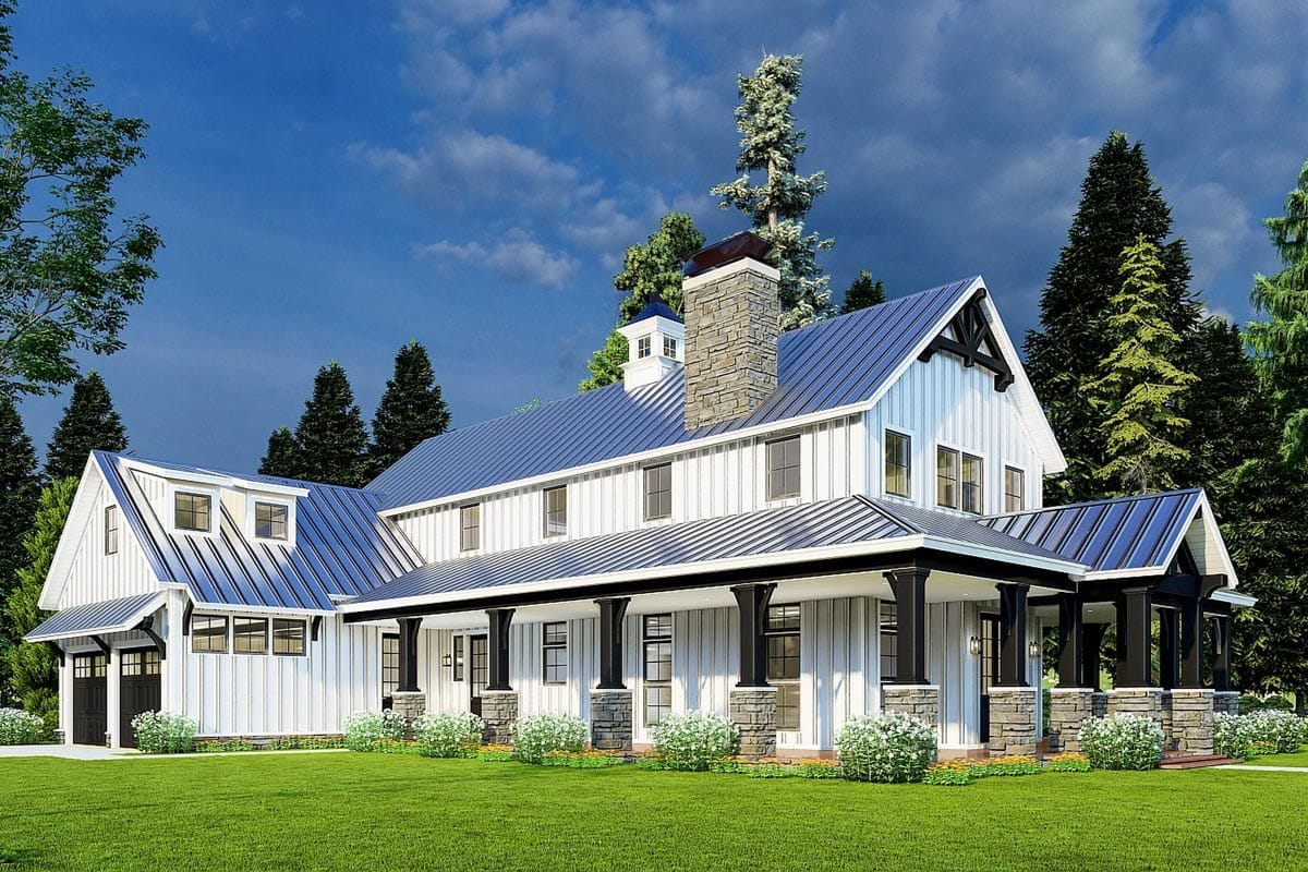 Front view of a 3-bedroom rustic house with a wraparound porch, stone chimney, white board-and-batten siding, and a blue metal roof, set among green lawn and tall trees, illustrating the 3,014 sq. ft. rustic home plan with a two-story great room.