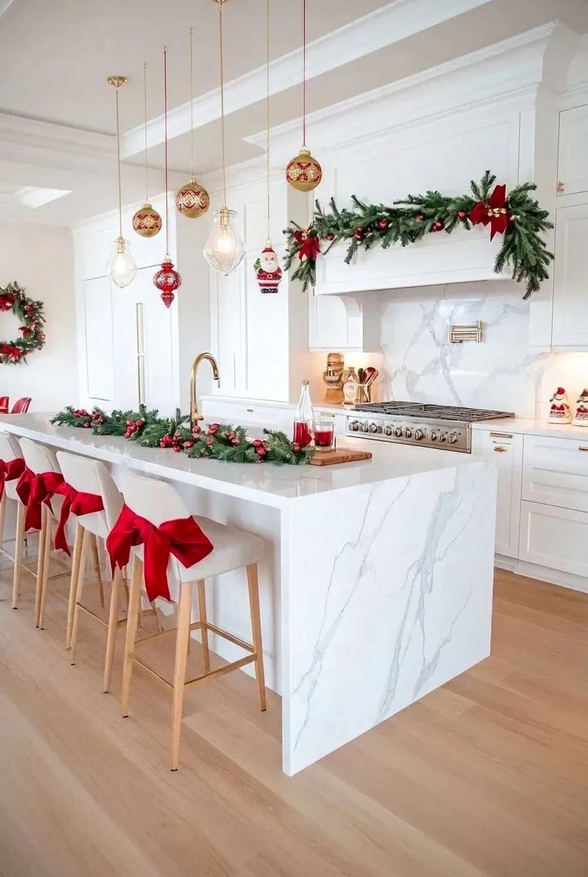 Christmas Kitchen Decor Ideas for a Kitchen You Still Have to Cook In 8 Modern white kitchen decorated for Christmas with garlands, red bows on bar stools, hanging ornaments, and festive wreaths, illustrating Christmas kitchen decor ideas for a functional cooking space.