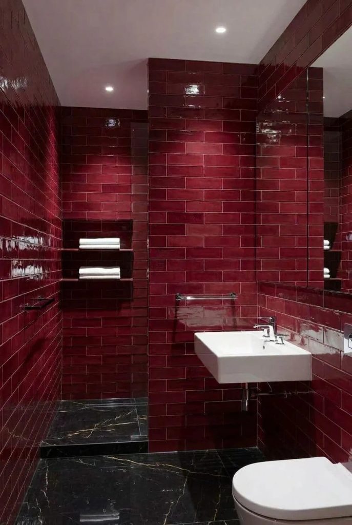 Bathroom 2 Modern bathroom featuring glossy burgundy subway tiles on the walls, black marble floor with white veining, a white floating sink, and a wall-mounted toilet, illustrating bold burgundy bathroom ideas with rich tile texture and sleek finishes.