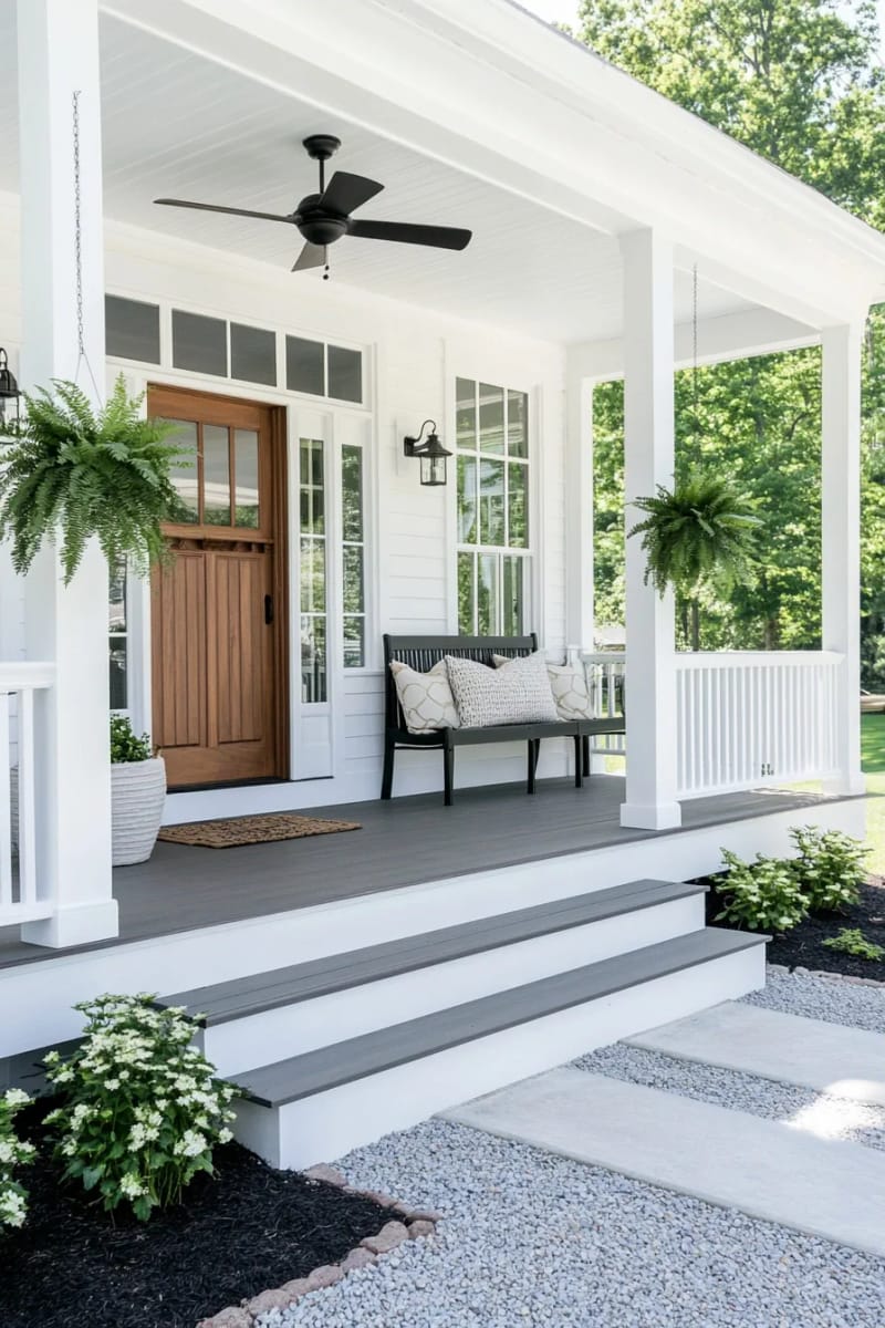 white farmhouse porch with staircase, hanging ferns, and black bench. 1