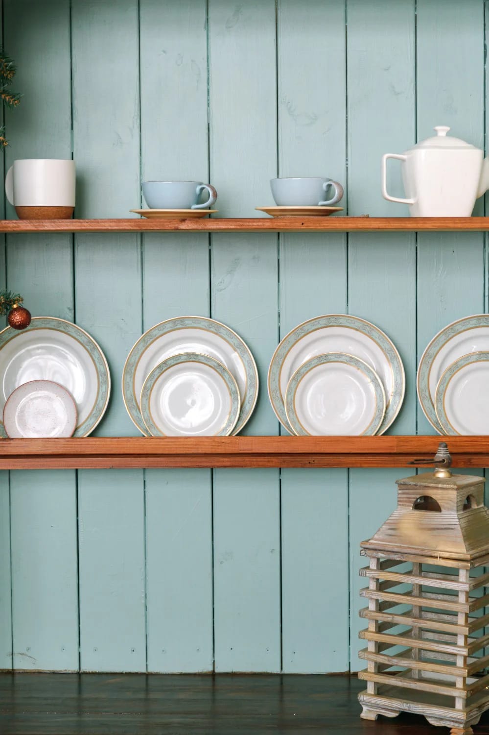 13 Kitchen Color Ideas and Where Each One Actually Works 25 Open wooden kitchen shelves displaying dishes and cups in front of a soft teal painted plank wall, illustrating kitchen color ideas that do not involve the cabinets.