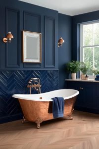 Navy Blue Bathroom Ideas, and Where the Navy Should Actually Go 10 Elegant bathroom featuring navy blue paneled and tile walls, a freestanding copper bathtub with navy towel, gold fixtures, wooden herringbone floor, and natural light from a large window, illustrating navy blue bathroom ideas with warm copper accents.