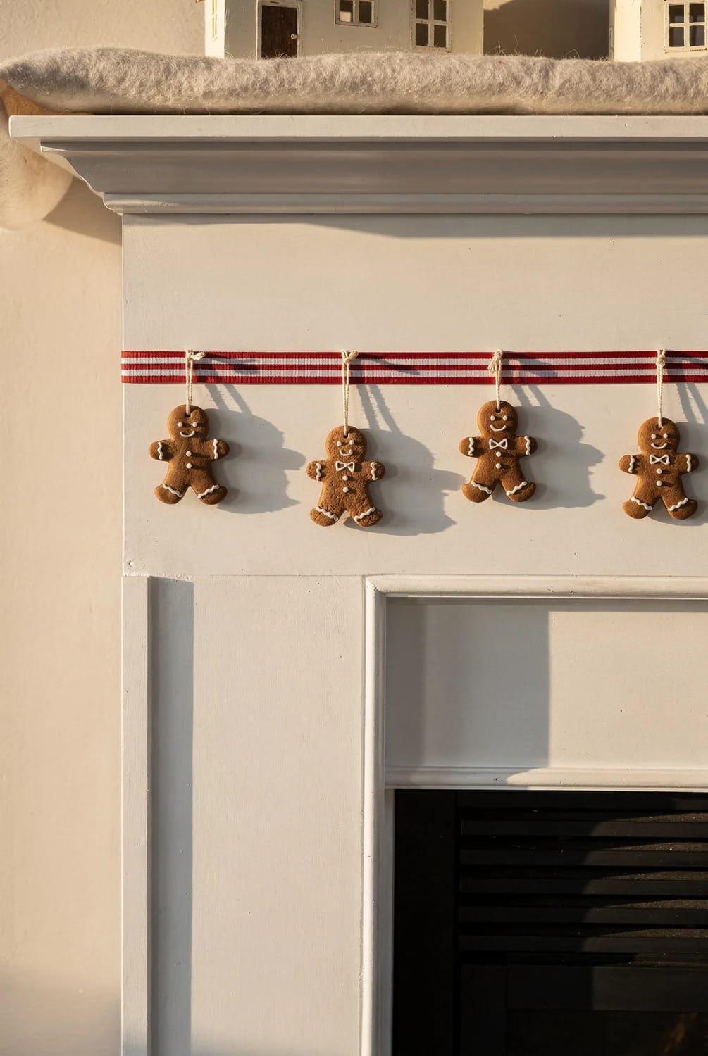 A white fireplace mantel with a red-and-white striped ribbon holding four decorated gingerbread figures before additional candy Christmas mantel decor is added