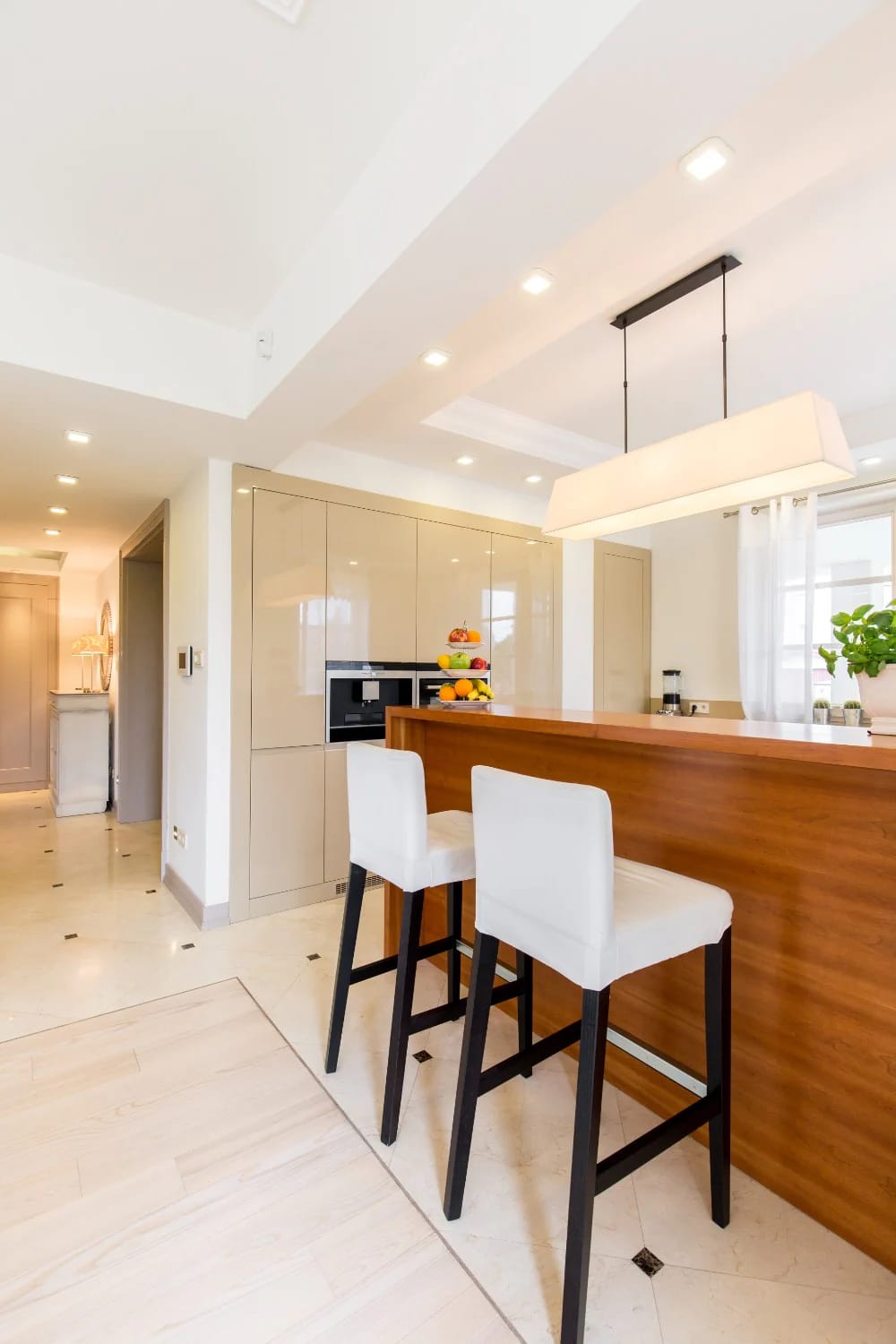 Kitchen Island With Dining Table: 11 Combinations That Actually Get Used 6 Modern kitchen island with a wooden dining table surface and two white upholstered stools, under a rectangular pendant light, illustrating a practical kitchen island with dining table combination.