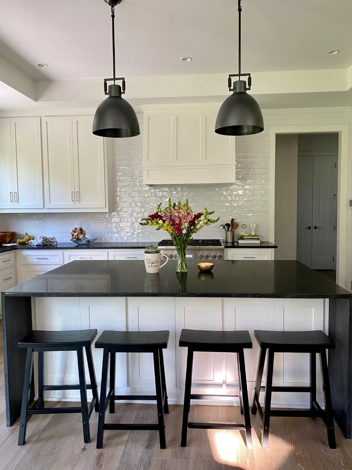 Kitchen Island With Dining Table: 11 Combinations That Actually Get Used 22 Modern kitchen featuring a kitchen island with four black stools, a dark countertop, and two pendant lights above, illustrating a kitchen island with dining table combination and distinct lighting zones.