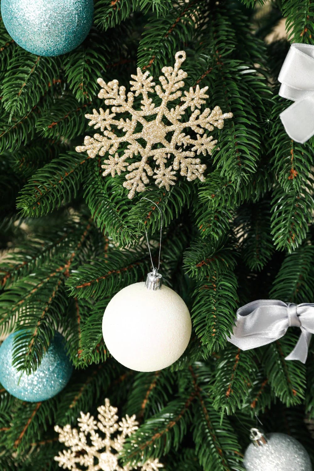 Scandinavian Christmas Decor With Pale Wood and Straw Ornaments That Reads Nordic, Not Rustic 17 Close-up of a Scandinavian Christmas tree decorated with pale wood-colored straw snowflake ornaments, white and blue baubles, and a silver ribbon, reflecting Nordic Christmas decor style.