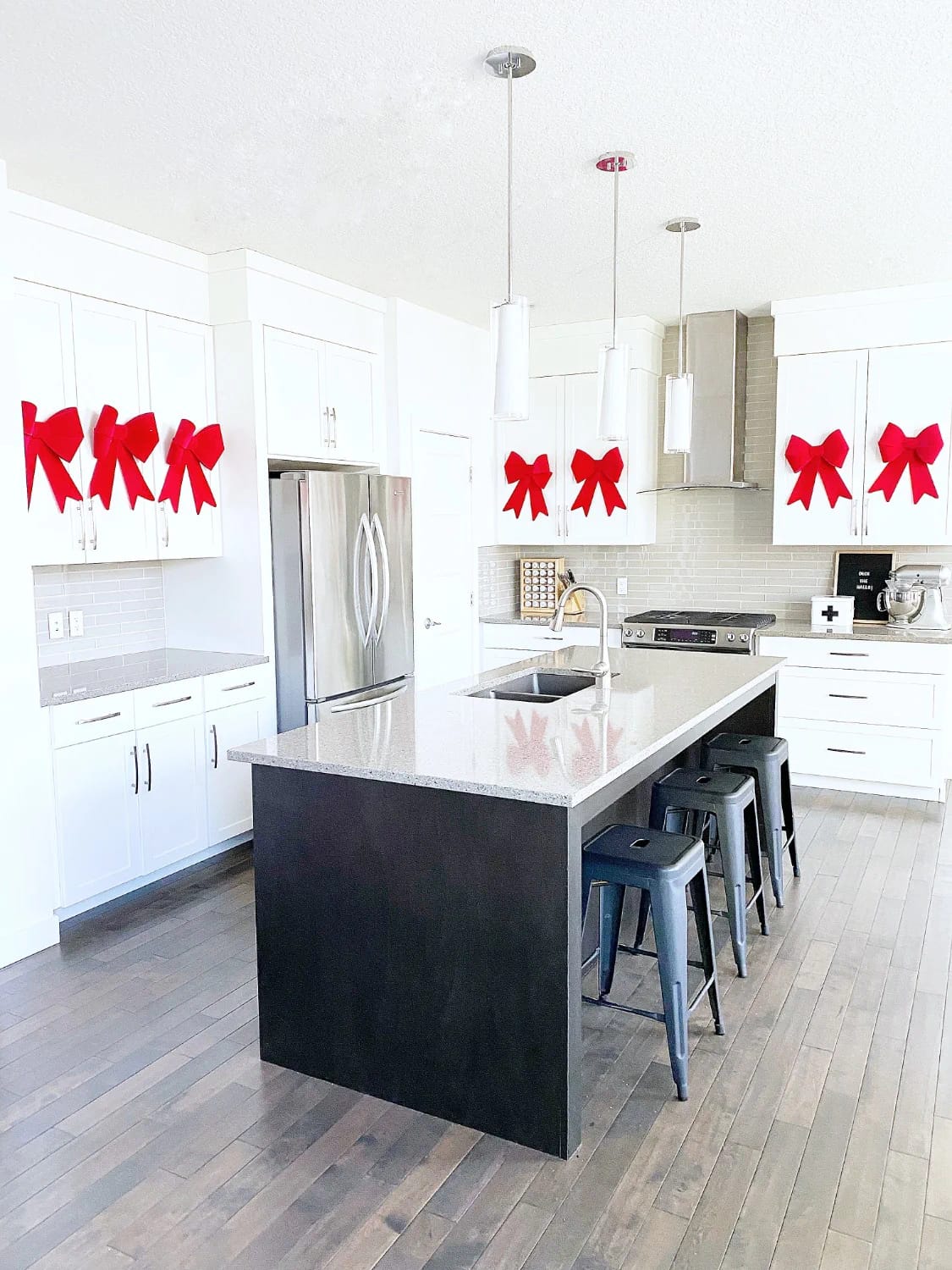 Modern white kitchen decorated with large red velvet bows attached to cabinet knobs, showcasing a festive red ribbon Christmas decor idea beyond the tree.