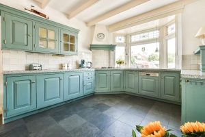 Bright kitchen featuring sage green cabinets with unlacquered brass hardware, white tile backsplash, granite countertops, and large windows letting in natural light, illustrating sage green kitchen cabinets with unlacquered brass hardware.