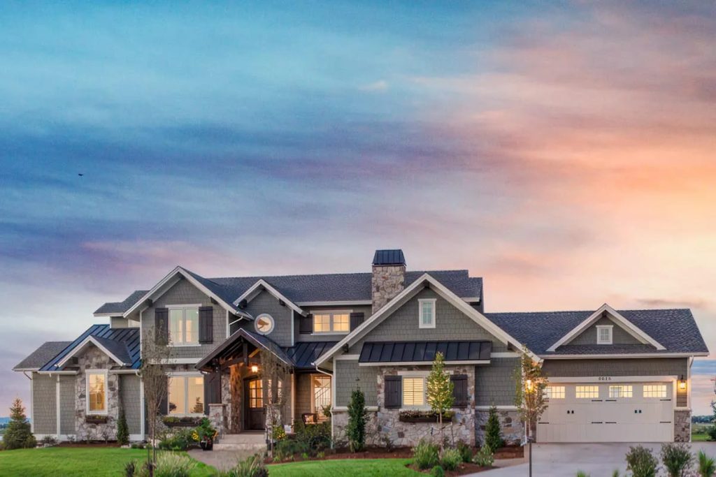 Craftsman-style home with gray shingle siding, stone accents, and multiple gables at sunset