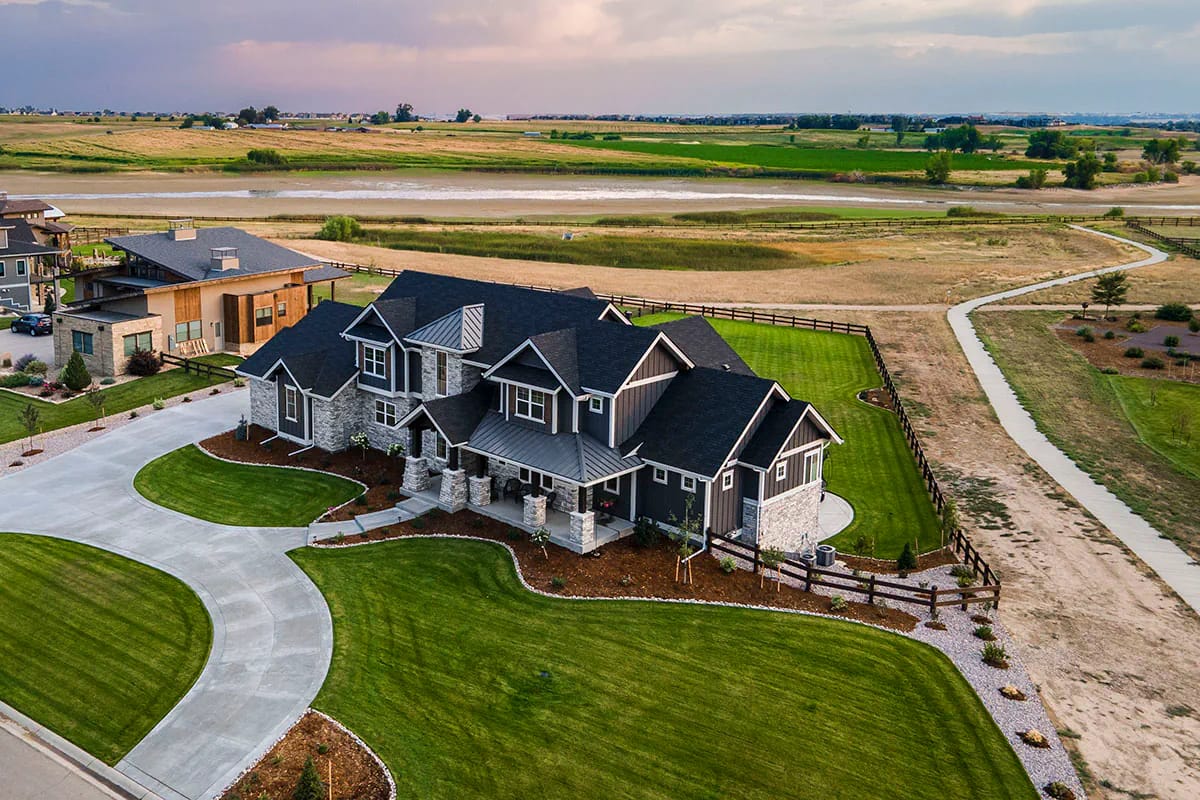 Aerial view of a two-story home with stone and siding exterior, gabled roof, and wraparound lawn