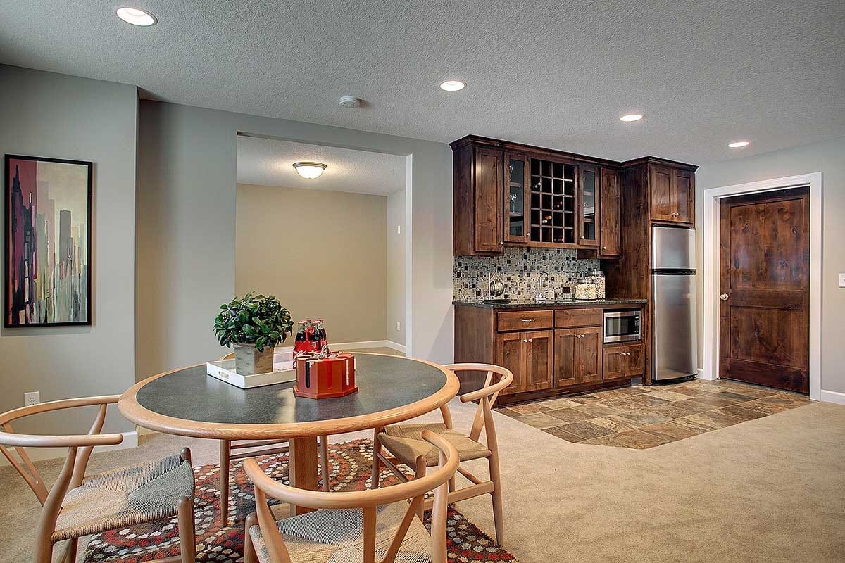 Basement wet bar with dark wood cabinetry, mosaic backsplash, and a round dining table with modern chairs.