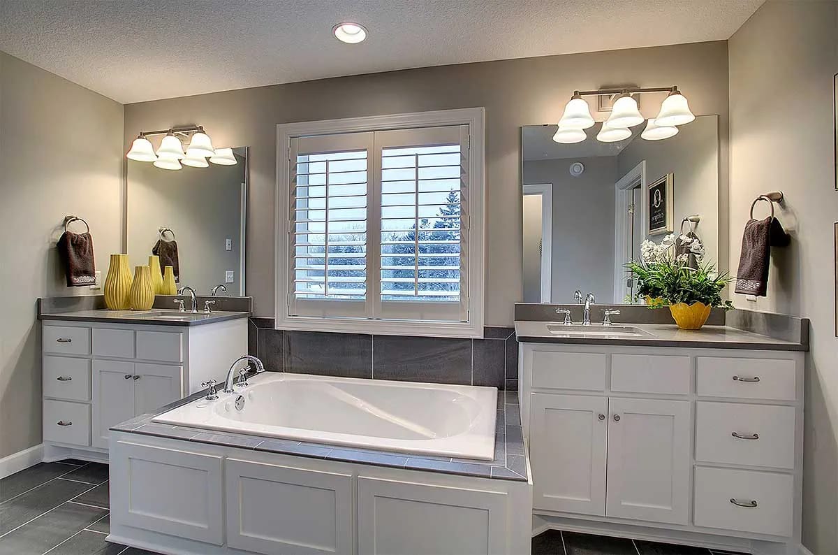 Bathroom with soaking tub, dual vanities, and large window with plantation shutters