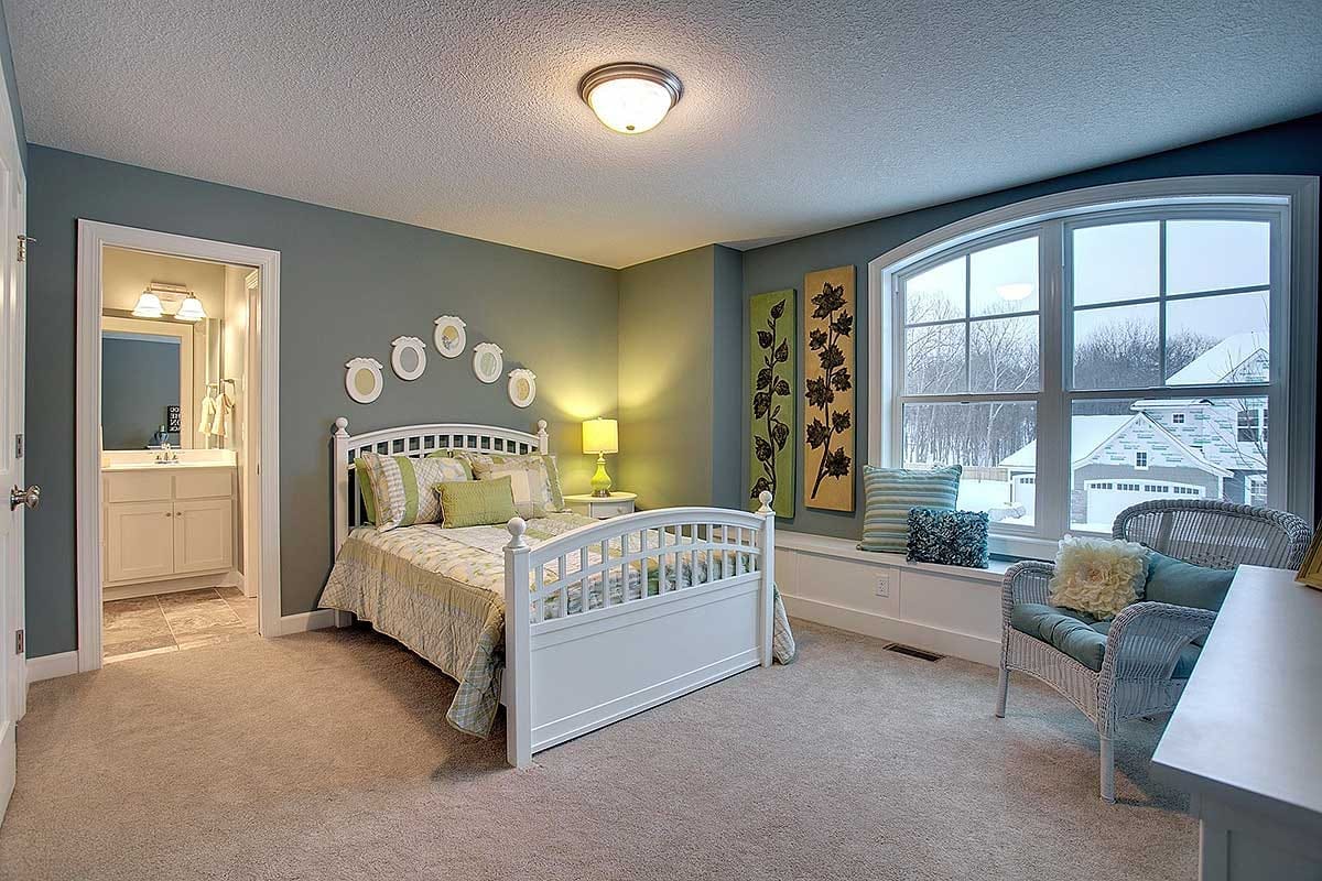 Bedroom with arched window seat, sage green walls, white spindle bed, and ensuite bathroom