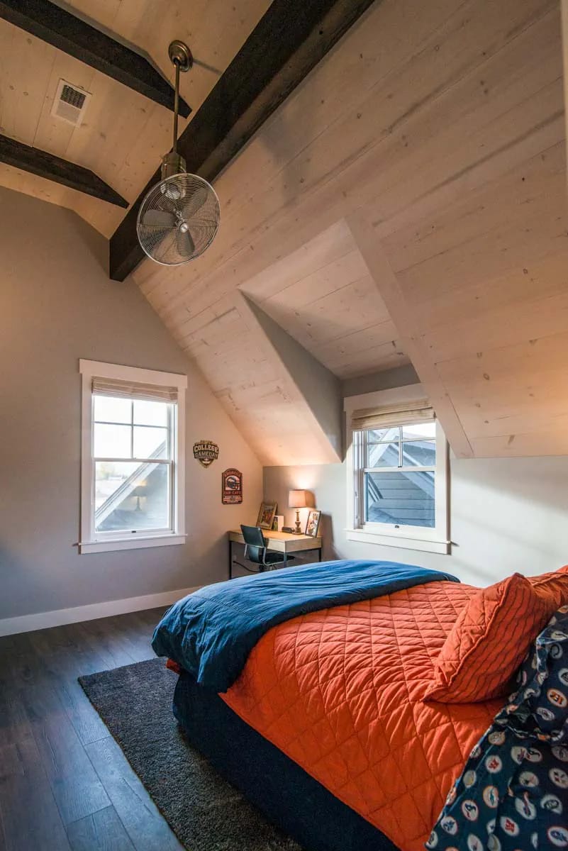 Bedroom with wood-paneled sloped ceiling, exposed beams, desk, and vibrant bedding