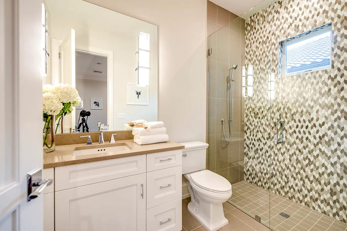 Bright bathroom with white vanity, glass shower, geometric tile accent wall, and neutral finishes