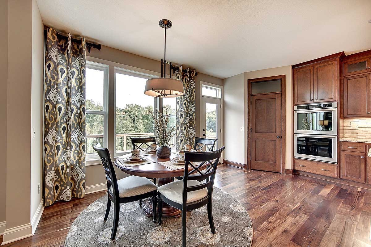 Bright breakfast nook with round table, patterned curtains, and warm wood kitchen cabinetry