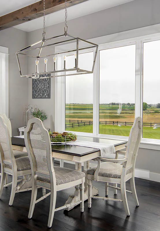 Bright dining area with farmhouse chairs, dark wood floor, and large windows overlooking countryside
