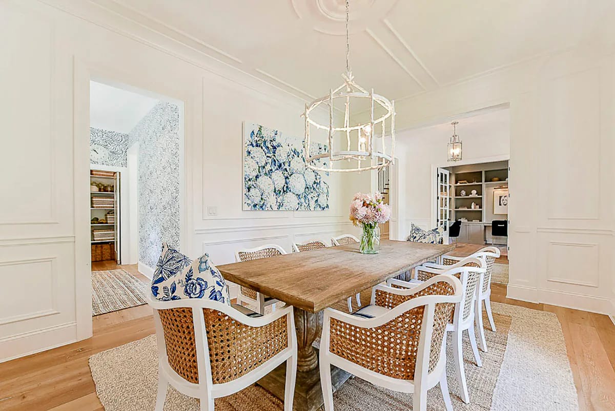 Bright dining room with wood table, rattan chairs, white walls, and a sculptural chandelier