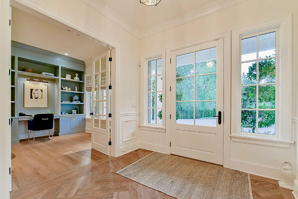 Bright entry hall with herringbone wood floor, glass French doors, and built-in home office shelving
