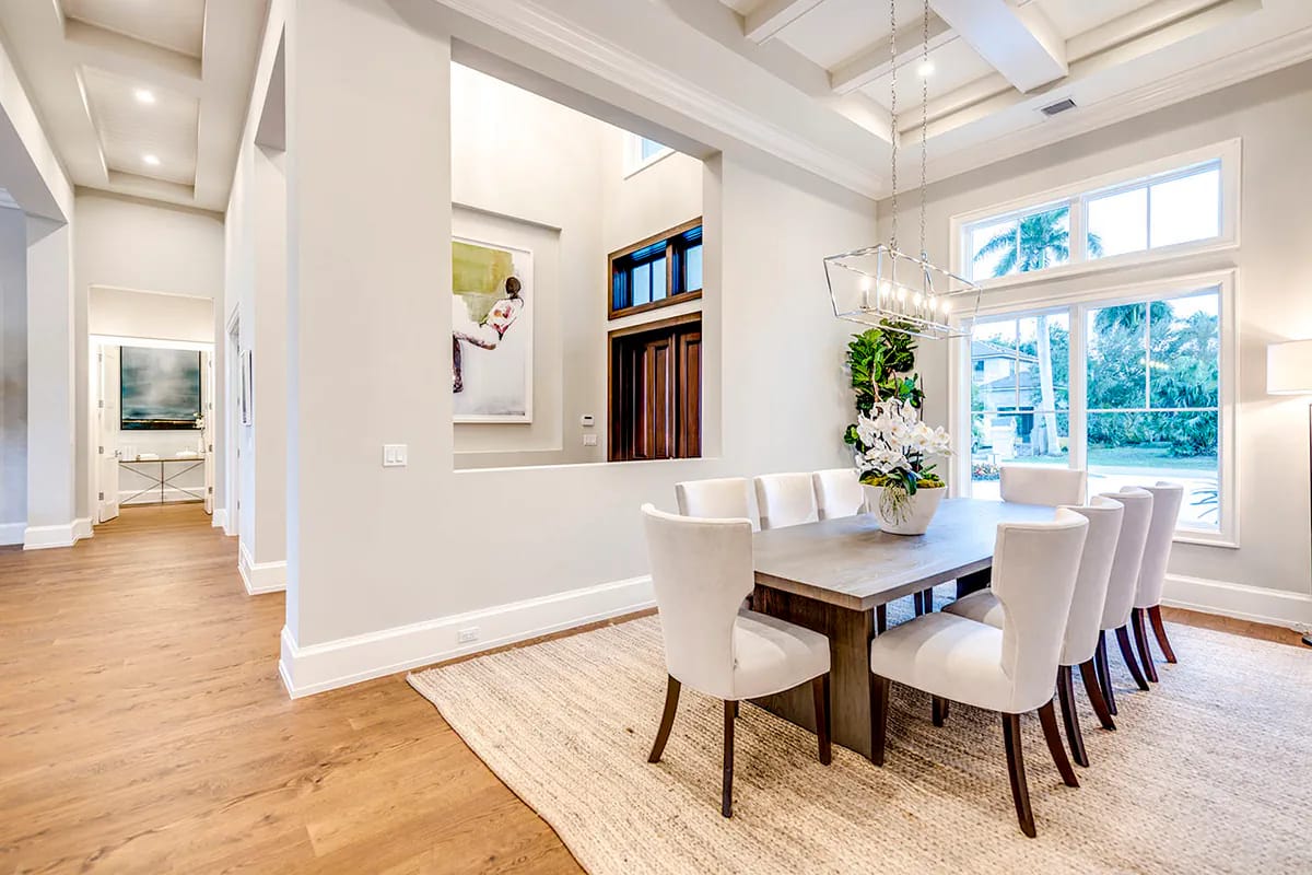 Bright formal dining room with coffered ceiling, wood table, upholstered chairs, and large garden-facing windows