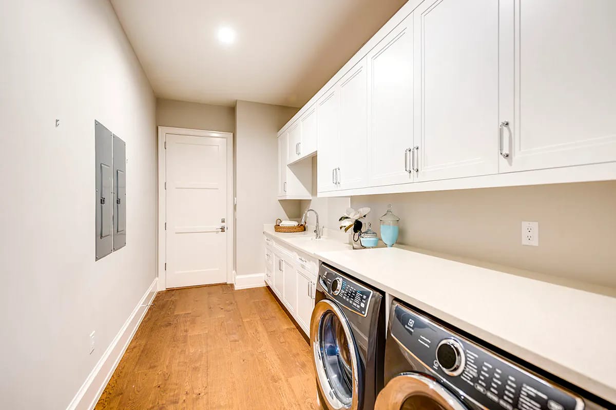 Bright laundry room with white cabinets, long countertop, front-load appliances, sink, and warm wood-look flooring