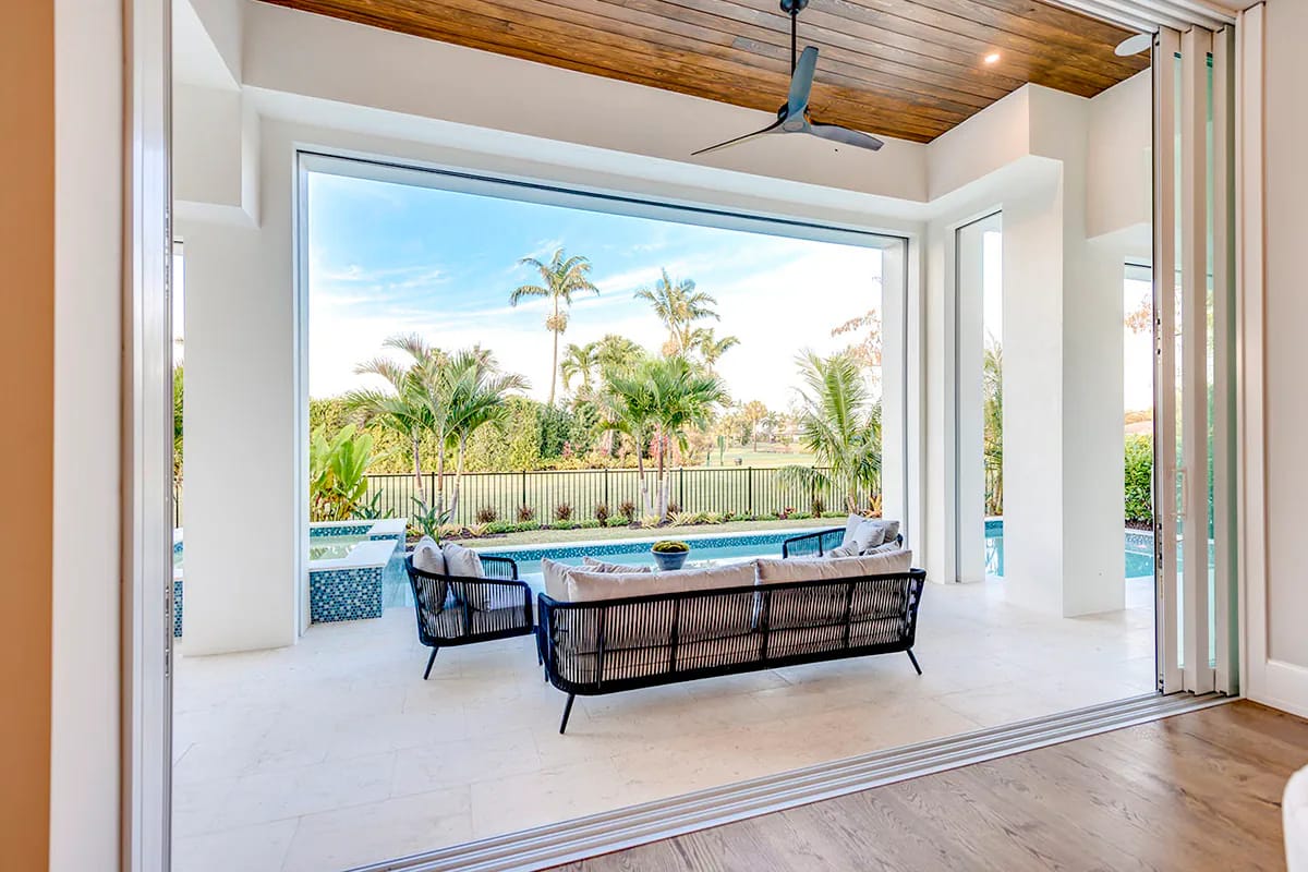 Bright living area opening to a covered terrace, pool, and tropical landscaped yard