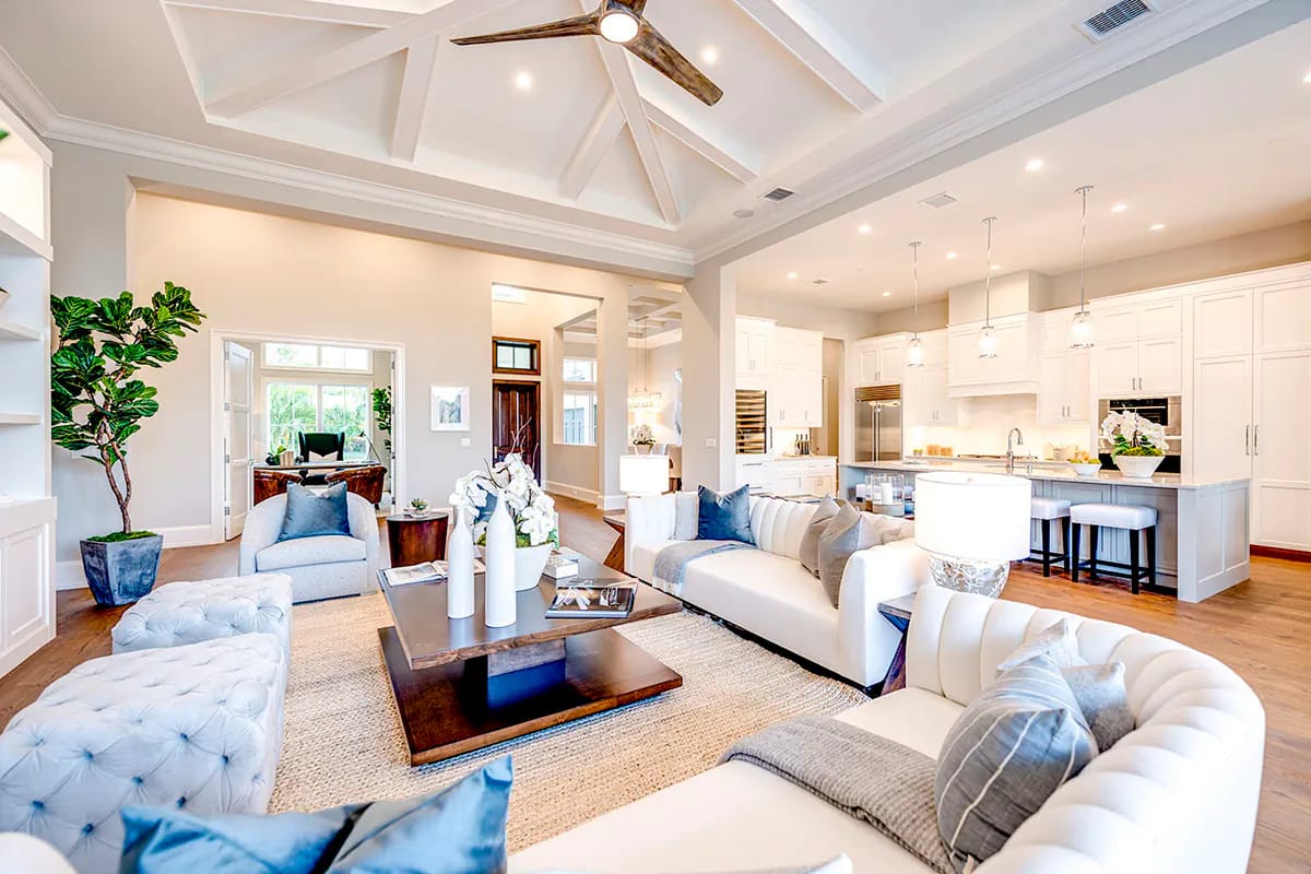 Bright open-concept living room and white kitchen beneath a coffered beam ceiling