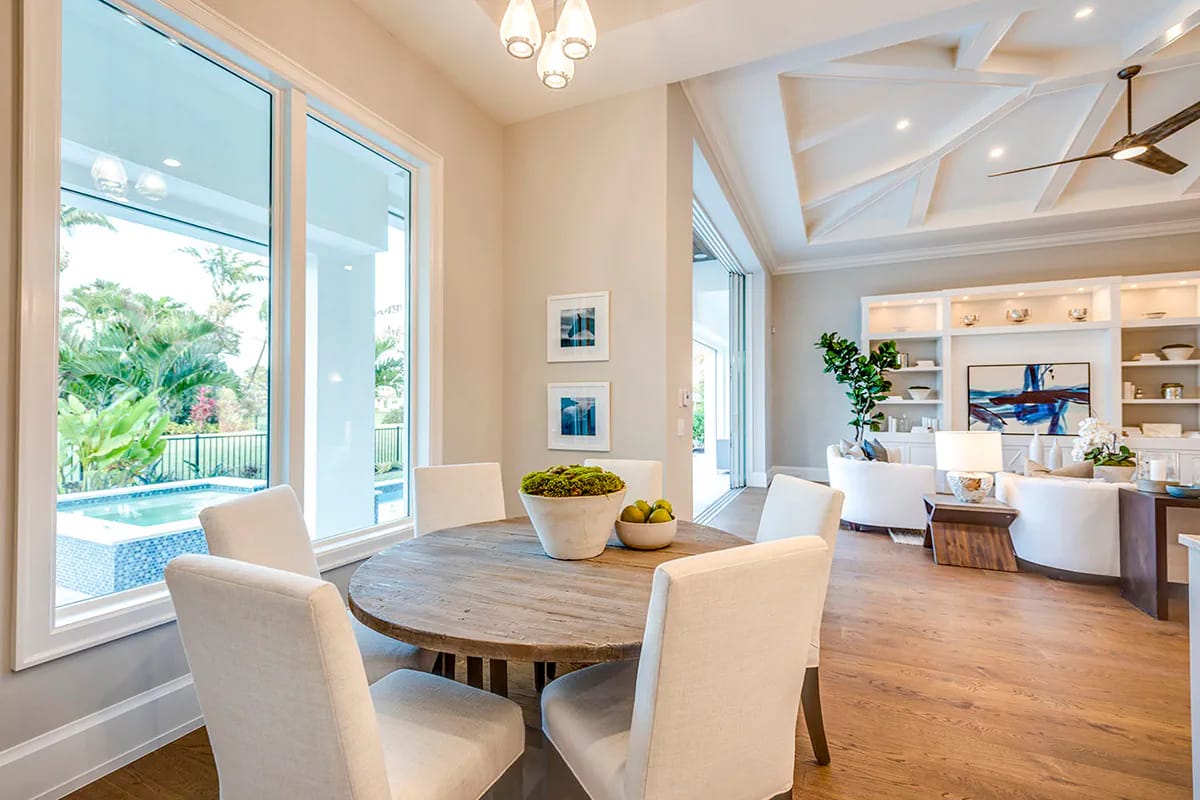 Bright open-plan dining and living room with pool views, coffered ceiling, and white built-in shelving