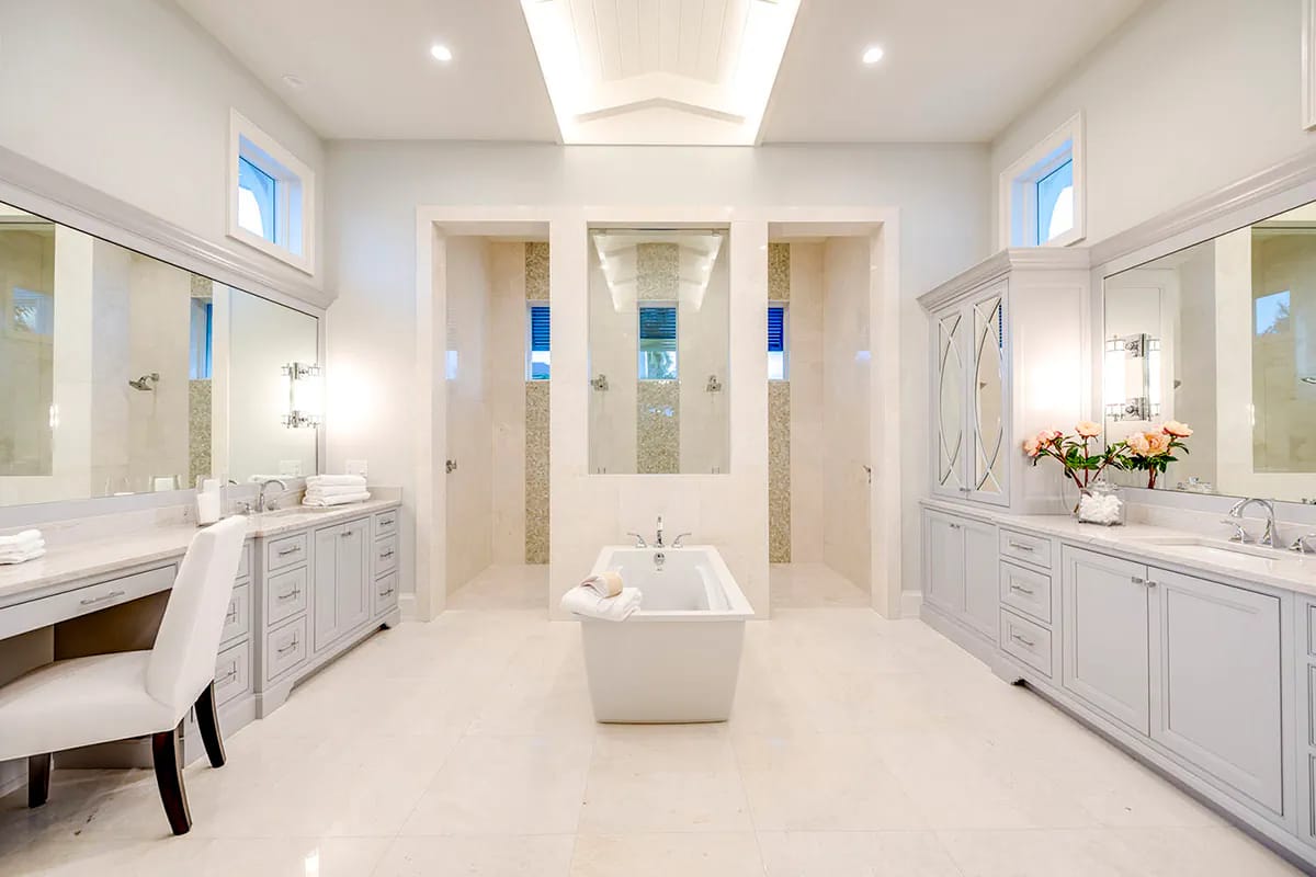 Bright symmetrical primary bathroom with freestanding tub, twin showers, vanities, and makeup station
