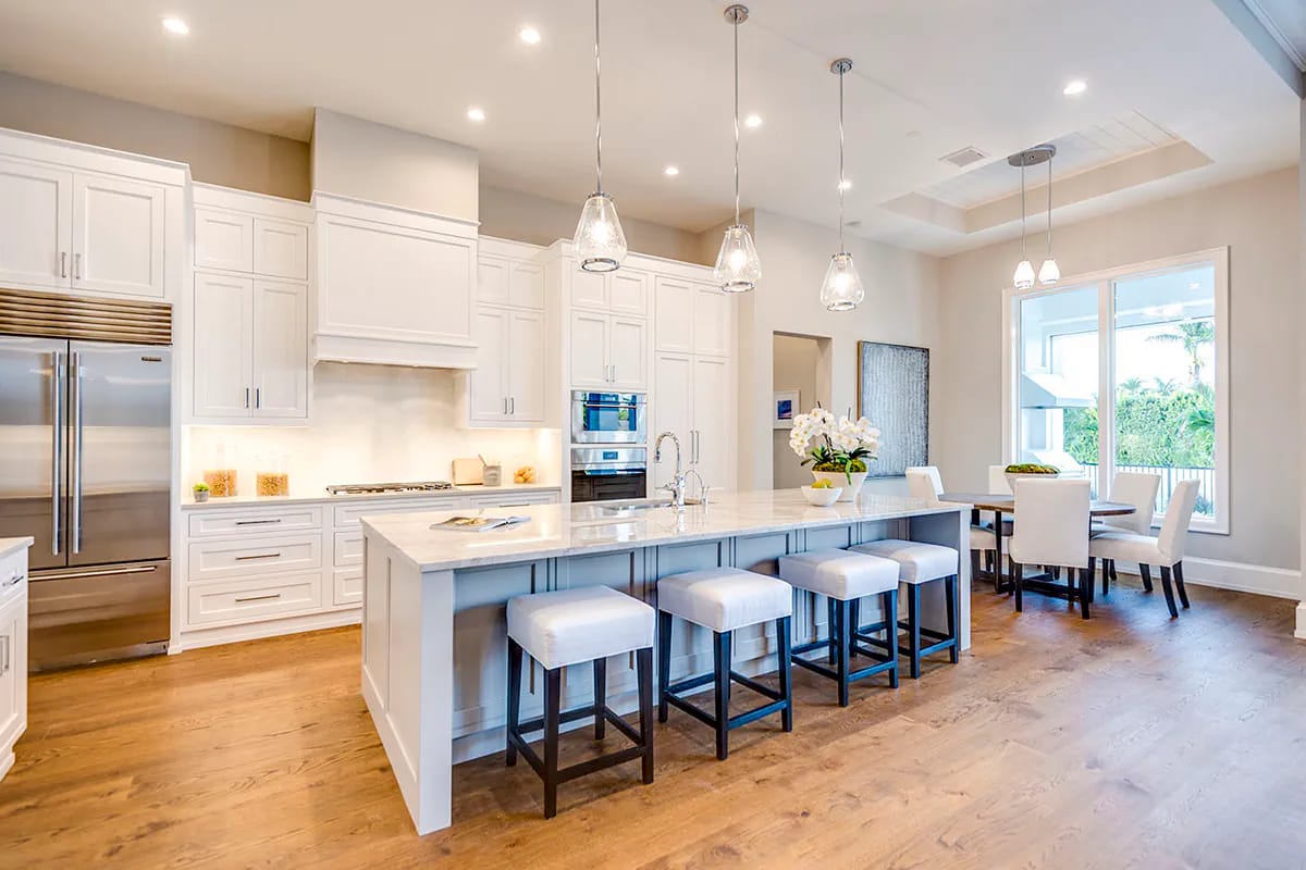 Bright white kitchen with large island, pendant lights, stainless appliances, and adjacent windowed dining area