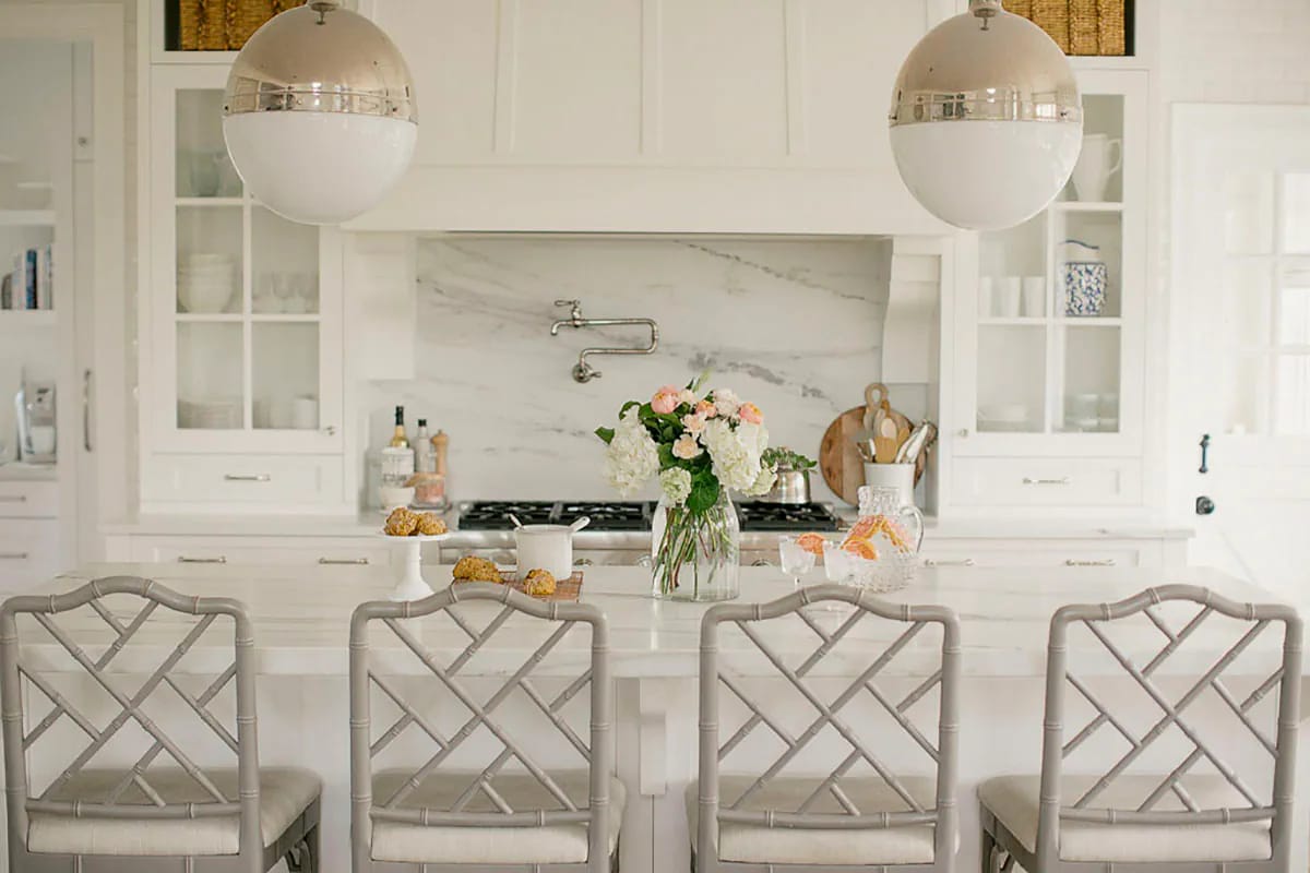 Bright white kitchen with marble island, globe pendants, and glass-front cabinetry