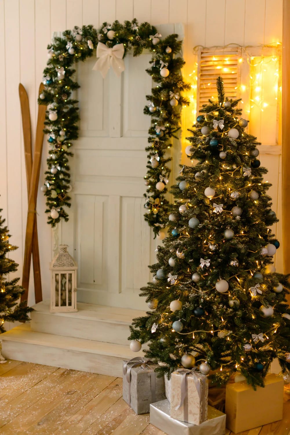 Two decorated, lighted Christmas garlands frame the sides and top of a white interior doorway, with a decorated Christmas tree and wrapped gifts in the foreground