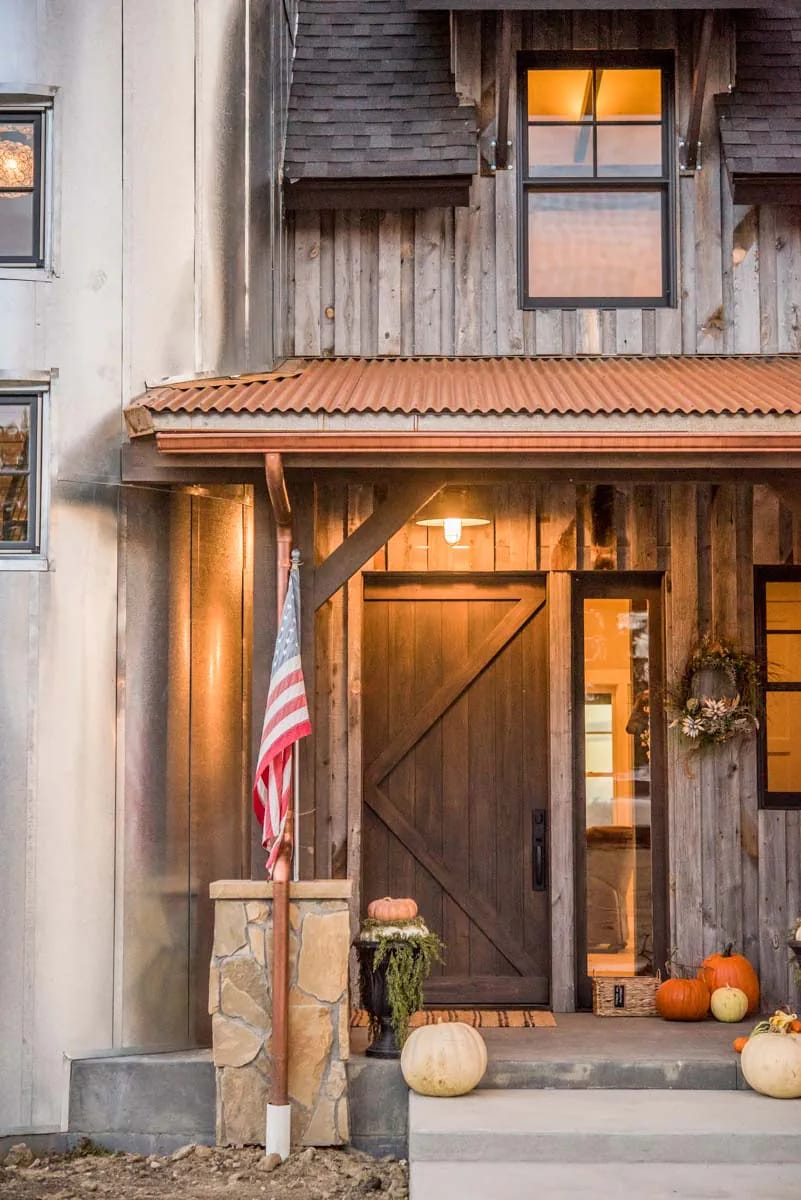 Close-up of rustic front entry with wood siding, barn door, metal roof, and stone column