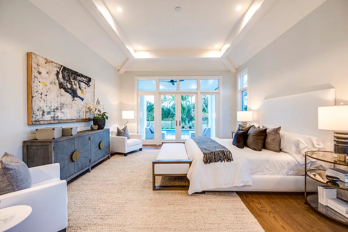Contemporary bedroom with tray ceiling, upholstered bed, abstract art, and glass doors opening to a pool view