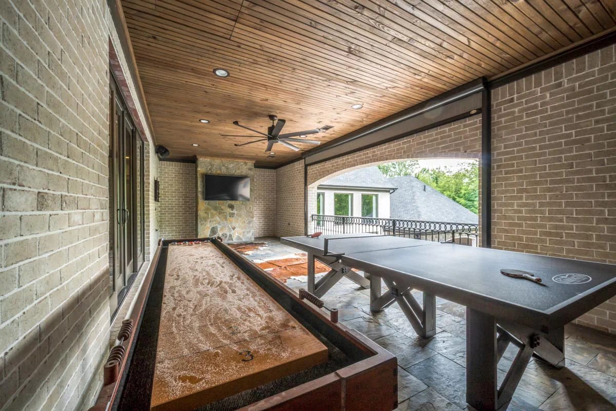 Covered gallery with shuffleboard and ping pong tables, wood ceiling, and stone accent wall with TV