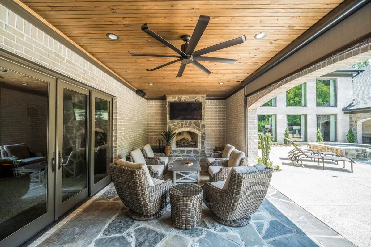 Covered outdoor living area with stone fireplace, wicker seating, and wood plank ceiling