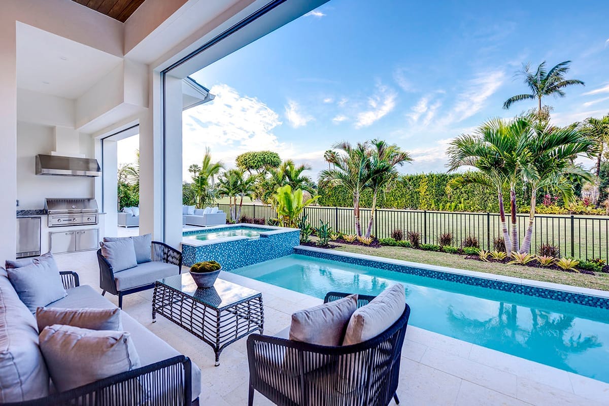 Covered outdoor lounge with grill, pool, raised spa, and tropical landscaping