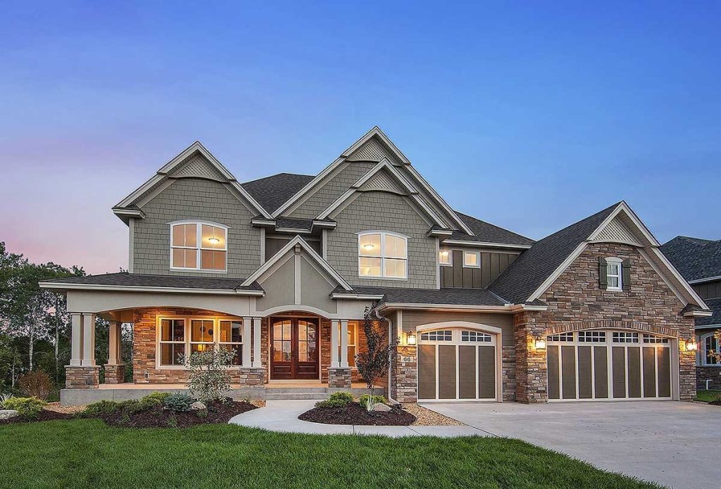 Craftsman-style home with gabled roof, stone and shingle siding, and a three-car garage at dusk