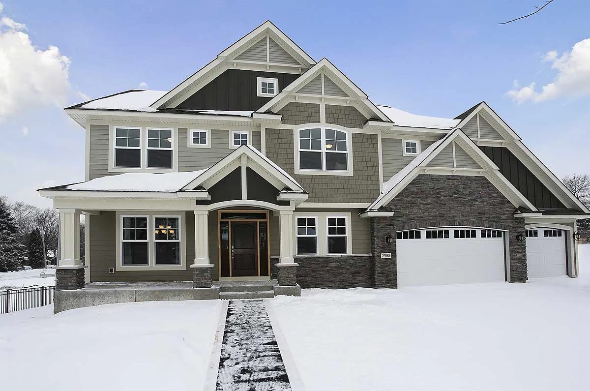 Craftsman-style two-story home with multiple gables, stone accents, and a three-car garage in a snowy setting.